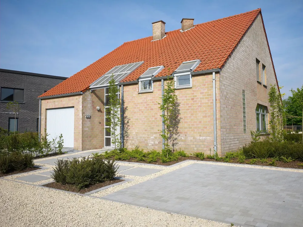 Allée et parking en pavés béton gris devant une maison belge en brique à toit de tuiles