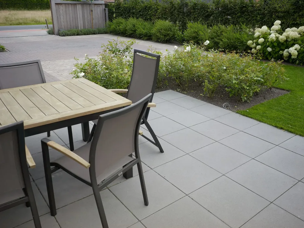 Terrasse en dalles béton clair avec table et chaises de jardin, pelouse et massif